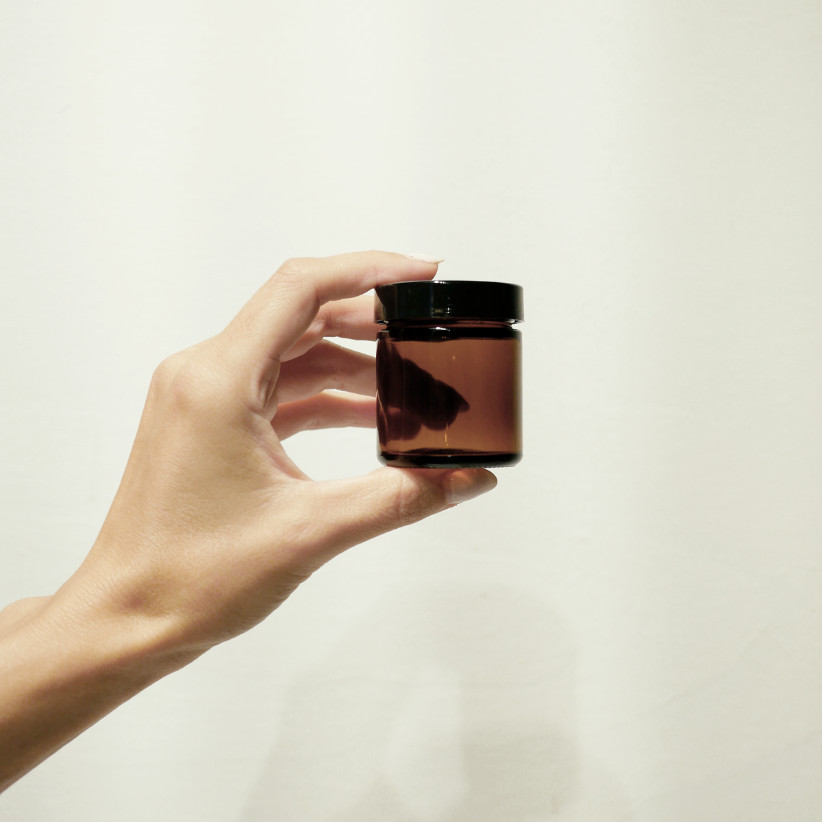 Hand holding a 2oz amber jar with a black twist off lid.