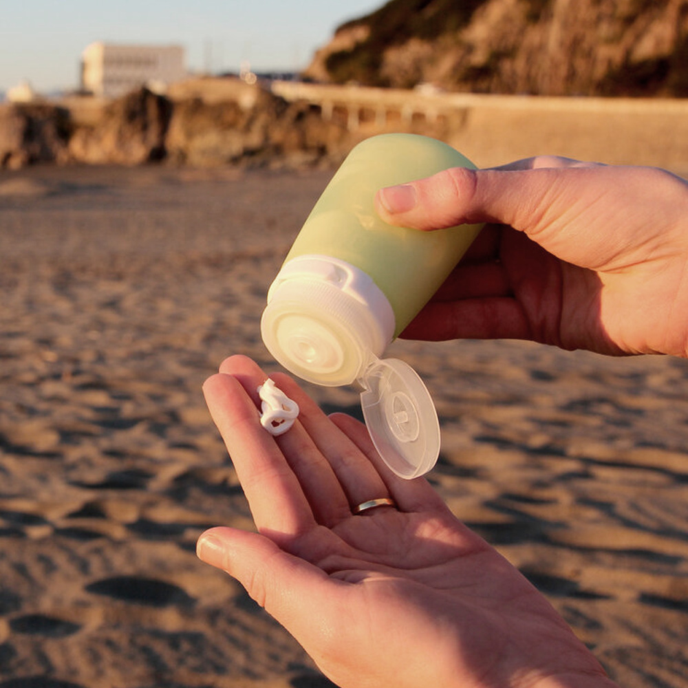 Lifestyle image on the beach of hands squeezing sunscreen out of a GoToob.