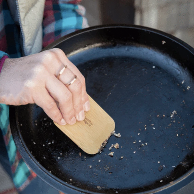 Up close image of a woman's hand scraping a dirty pot with a bamboo pot scraper.