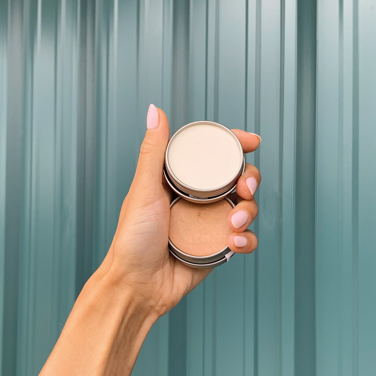 hand holding two tins of tinted and regular SPF 50+ mineral sunscreen butter.