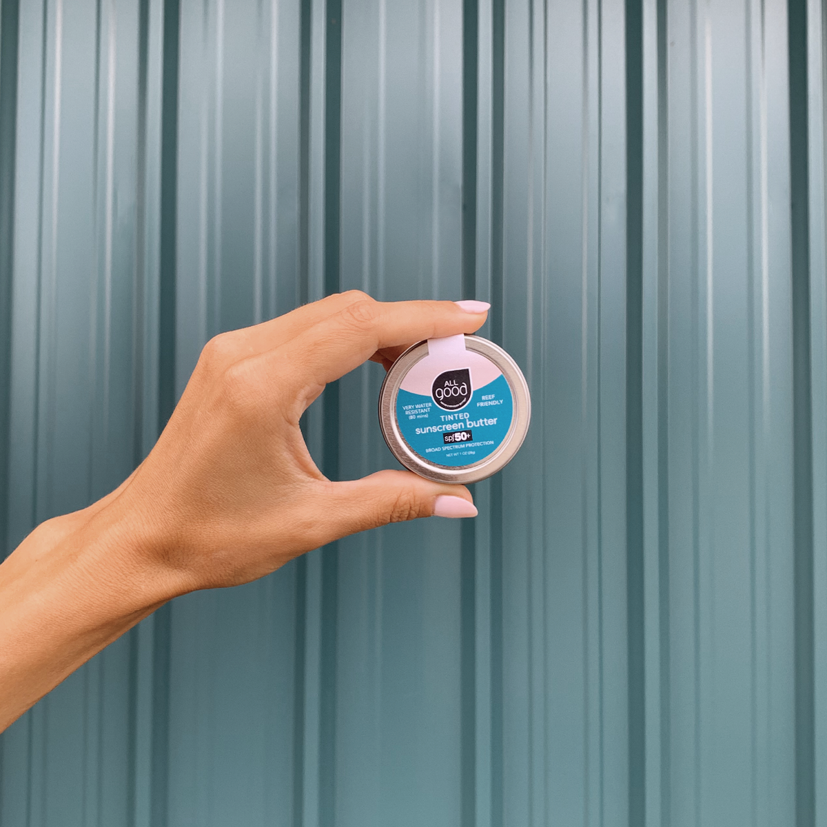 hand holding a 1oz aluminum tin of SPF 50+ tinted mineral sunscreen butter.