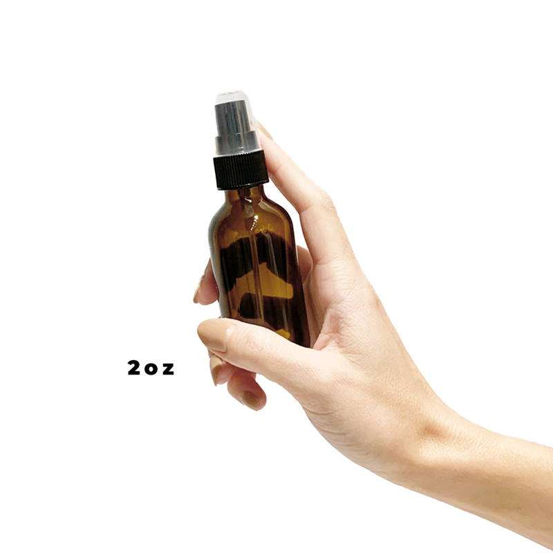 Hand holding a 2oz glass amber bottle with a black spray top.