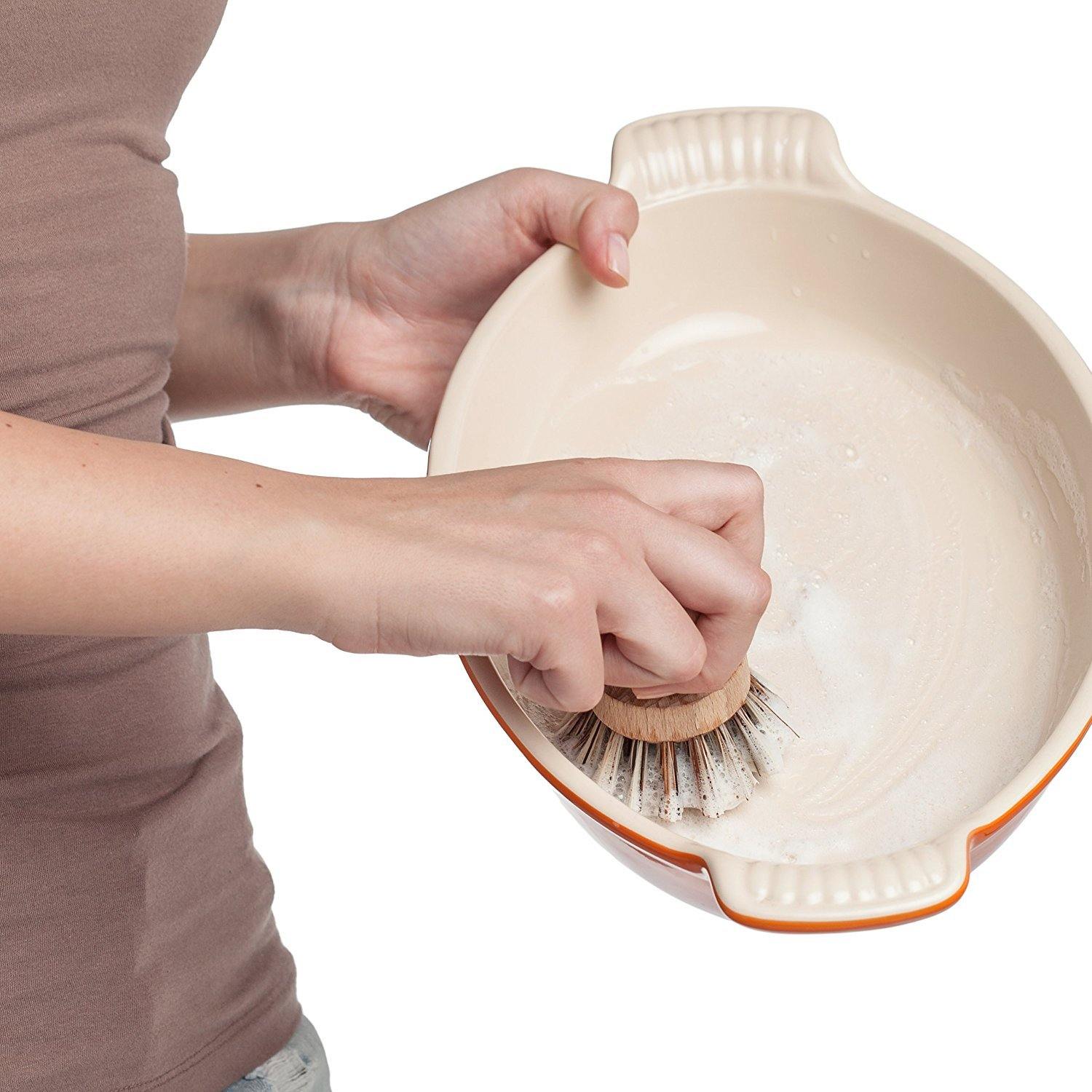 woman scrubbing a pot with the wooden pot brush.