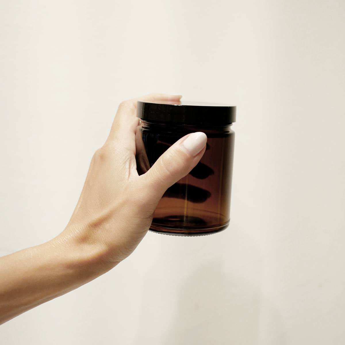 Hand holding an 8oz amber jar with a black twist off lid.