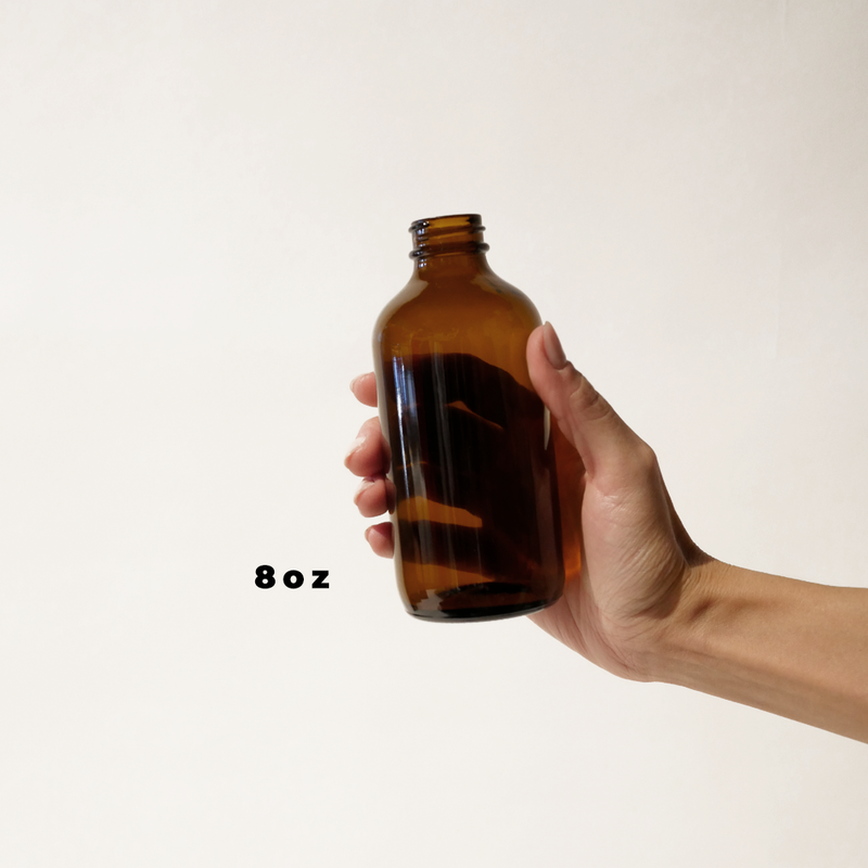 A hand holding an 8oz glass amber bottle for The Good Fill zero waste refills.