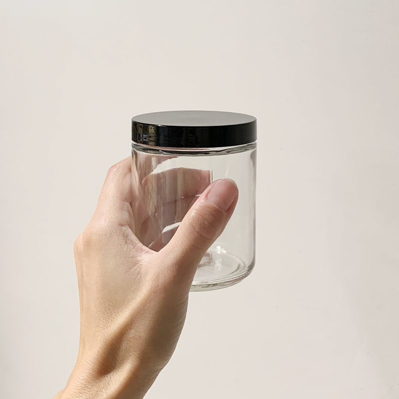 Hand holding a clear 9oz jar with a black screw-on lid.