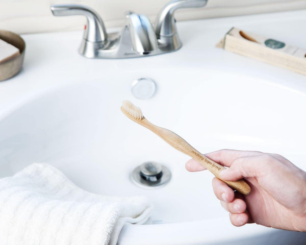 hand holding an adult sized zero waste bamboo toothbrush over a white bathroom sink