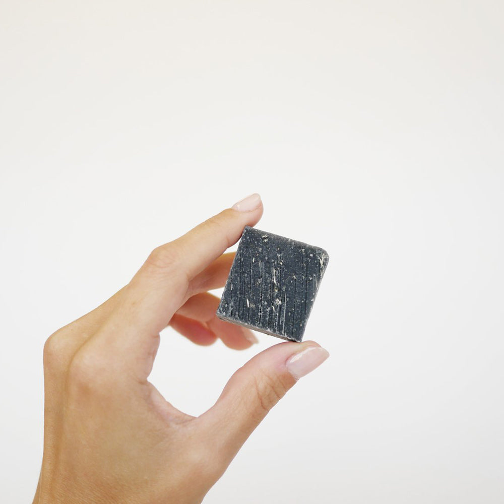 hand holding the small square, charcoal colored underarm detox bar.