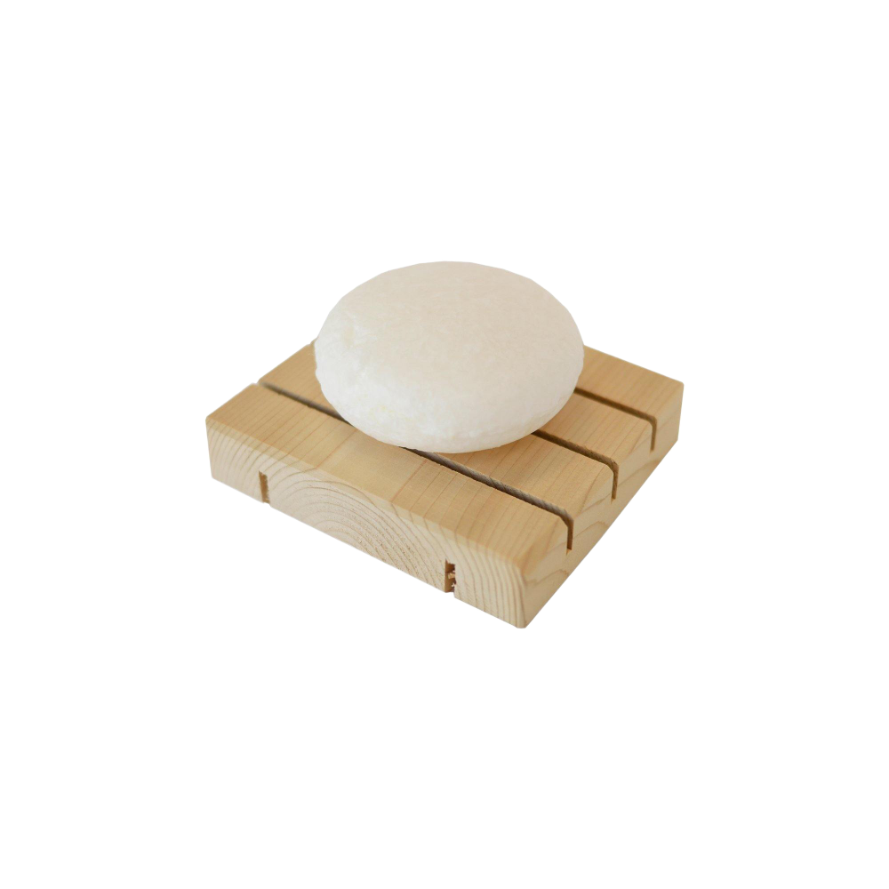 zero waste white, round dog shampoo bar sitting on a natural wooden soap dish.