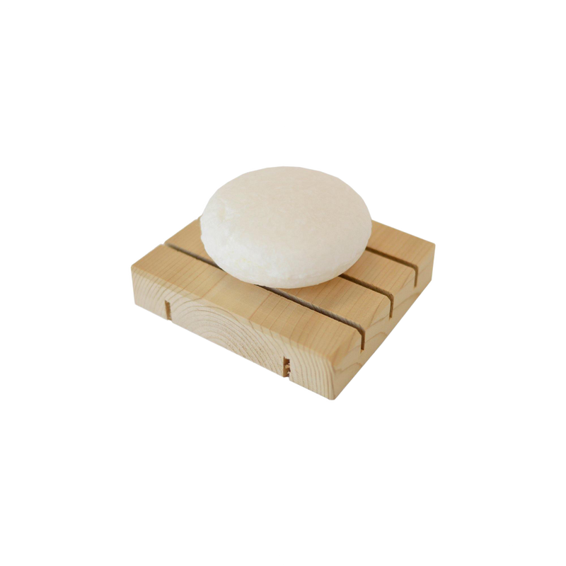 zero waste white, round dog shampoo bar sitting on a natural wooden soap dish.