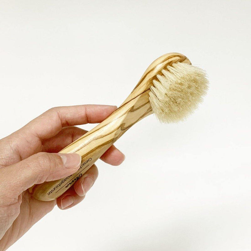 hand holding a natural wood face brush with natural white bristles