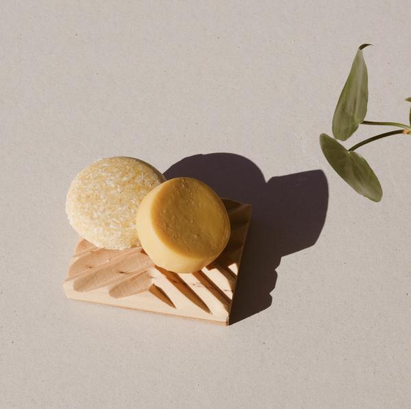 package free round yellow sweet citrus shampoo bar and round yellow sweet citrus conditioner bar sitting on a wooden soap dish