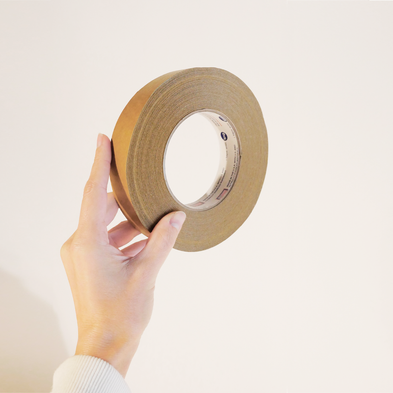 Hand holding a roll of brown recyclable kraft paper tape.