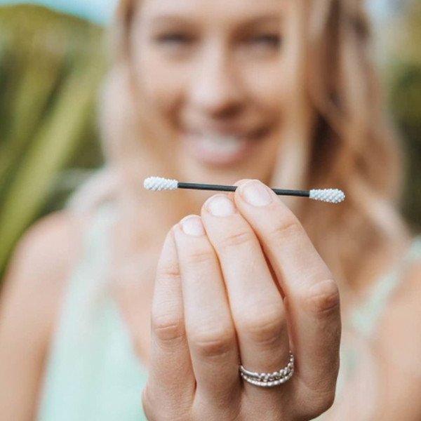 A woman holding up a reusable cotton swab. The swab is white on the ends with a black wand.