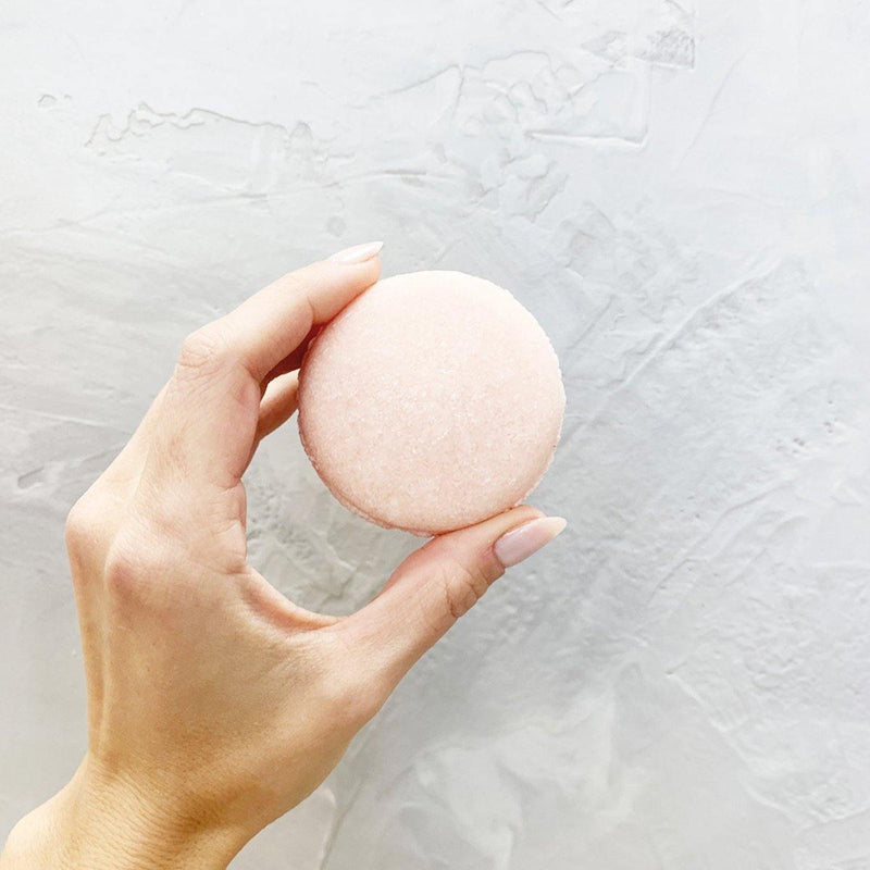hand holding a pink, round lavender cedar shampoo bar.