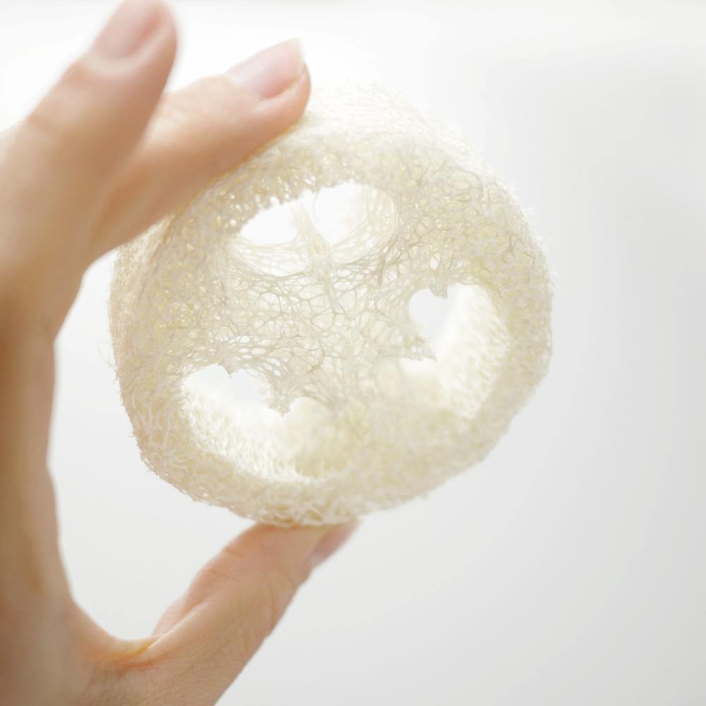 hand holding up a round, natural white loofah sponge.