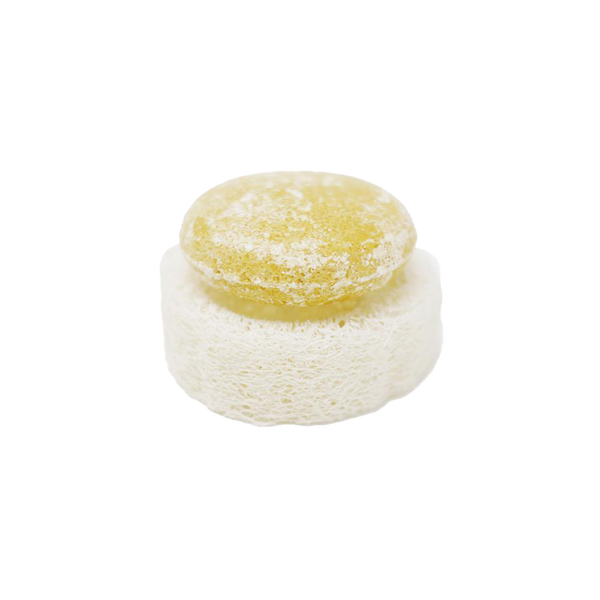 a round yellow shampoo bar sitting on top of a round zero waste and package free loofah. The loofah is a natural white color.