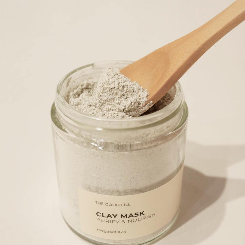 Small brown wooden spoon scooping light weight mask powder from a 4oz. reusable Good Fill glass jar.