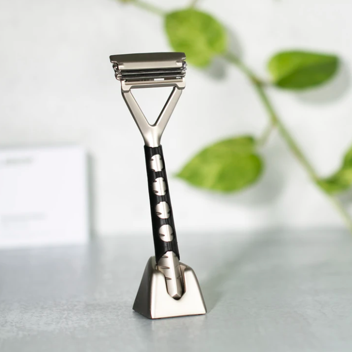 Black custom molded silicone grip sleeve on a silver leaf razor. The razor is sitting upright in a silver leaf stand.