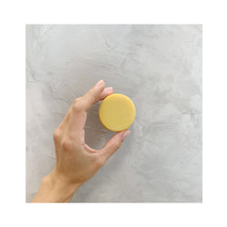 hand holding a yellow round zero waste sweet citrus conditioner bar