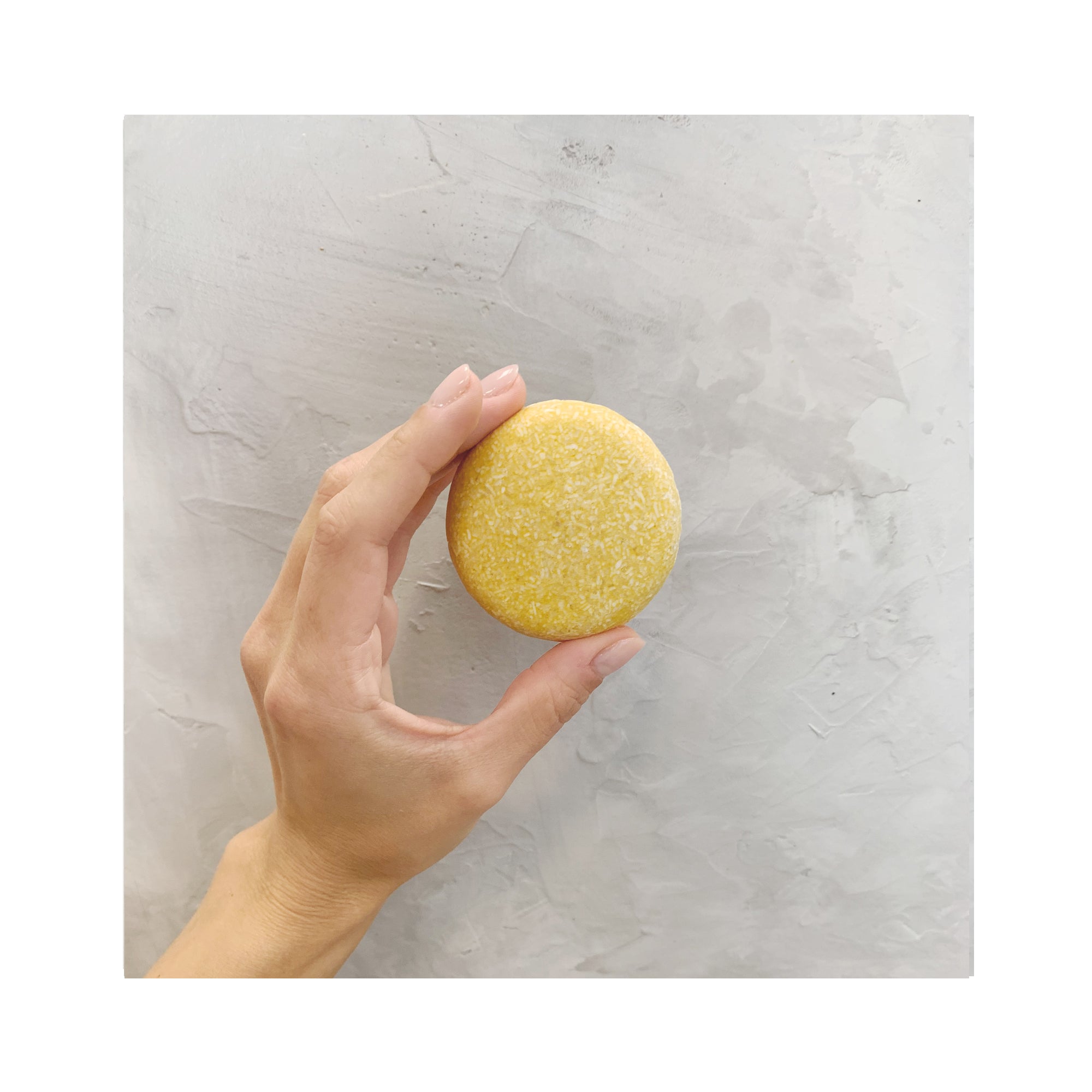 hand holding a yellow round zero waste sweet citrus shampoo bar
