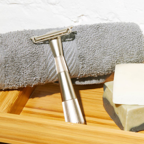 Silver twig safety razor for zero waste shaving.  The razor is sitting next to a grey bath towel and a bar of soap.